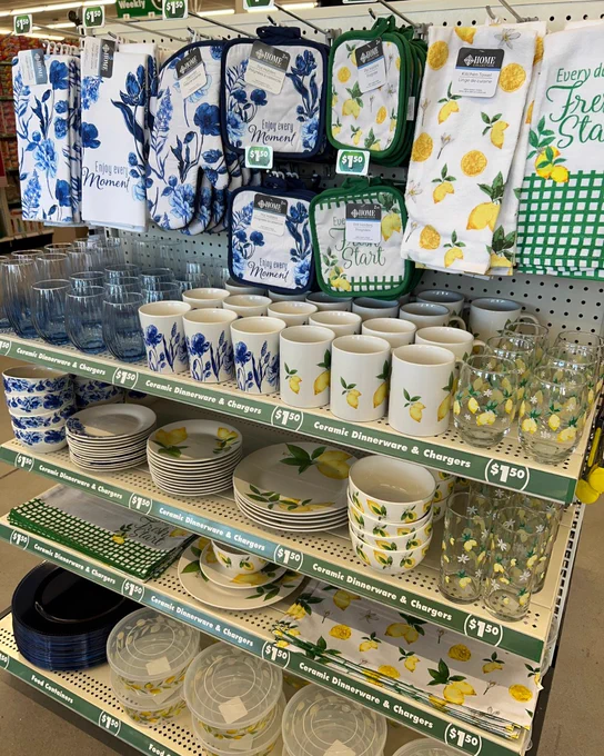 Kitchen textiles and ceramic dinnerware featuring blue floral and lemon patterns displayed on store shelves with price tags.