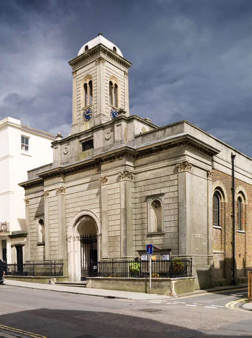 Georgian exterior of St. Andrew's Hove, a square white church, with turret and blue clock.
