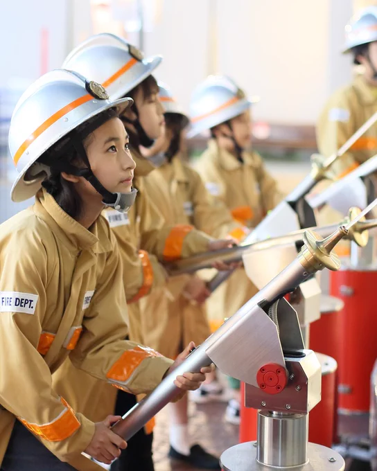 A photo of children wearing firefighter uniforms, aiming water hoses as they practice firefighting techniques. 