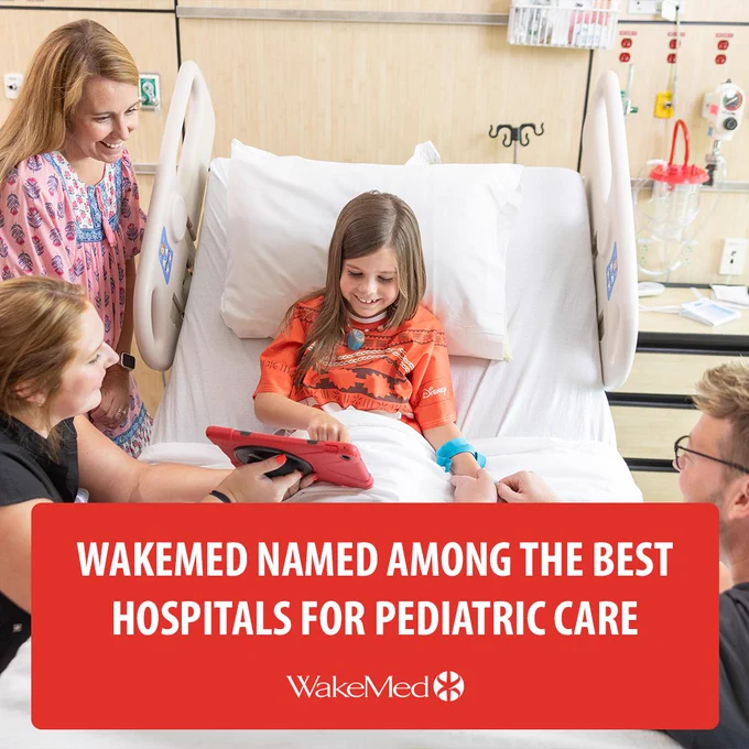 Child in hospital bed using a tablet, surrounded by supportive caregivers at WakeMed. Banner reads “WakeMed Named Among the Best Hospitals for Pediatric Care.”