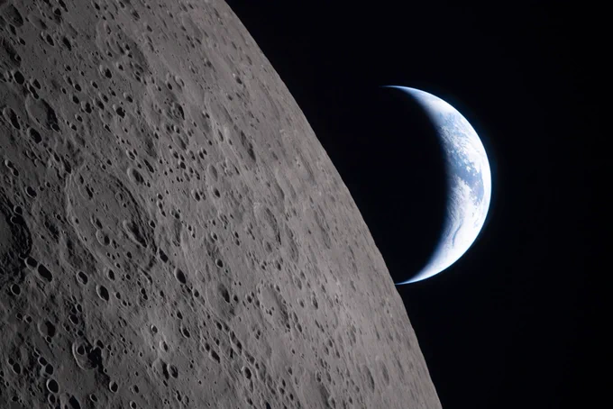A photo of the crescent Earth positioned next to the cratered edge of the Moon's surface.