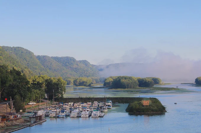 boats docked at a lake surrounded by hills and mist