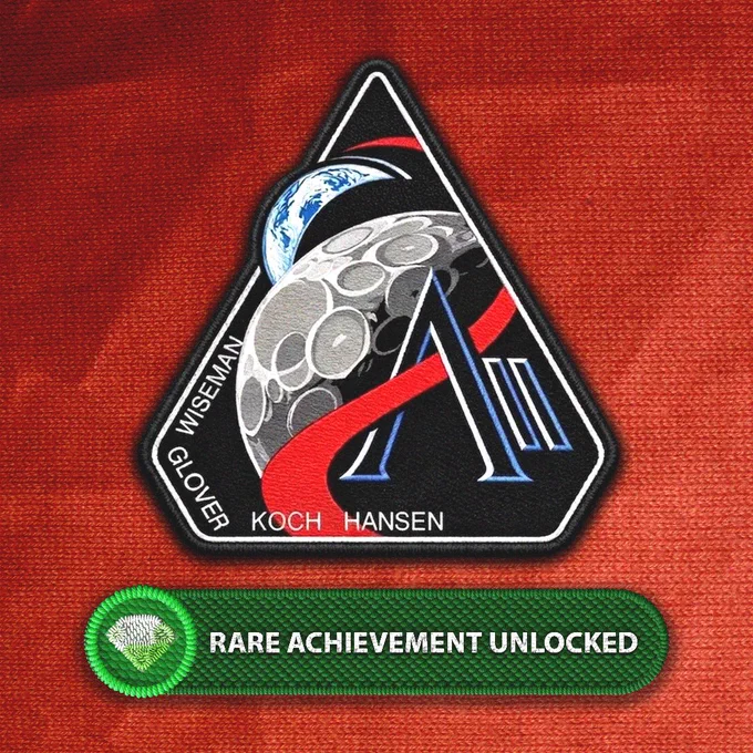 The NASA Artemis II mission patch is shown on an orange fabric background. Underneath is an embroidered patch of an Xbox Rare Achievement. Text on it reads "RARE ACHIEVEMENT UNLOCKED"