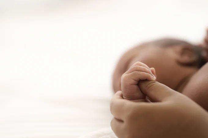 Close-up of a newborn baby's tiny hand gently grasping an adult's finger against a soft white background.