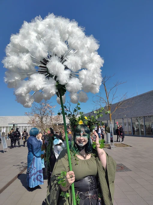 Cosplayerin  in grünem Kostüm mit Blätterranken, Blumen im Haar und einer riesigen Pusteblume. 