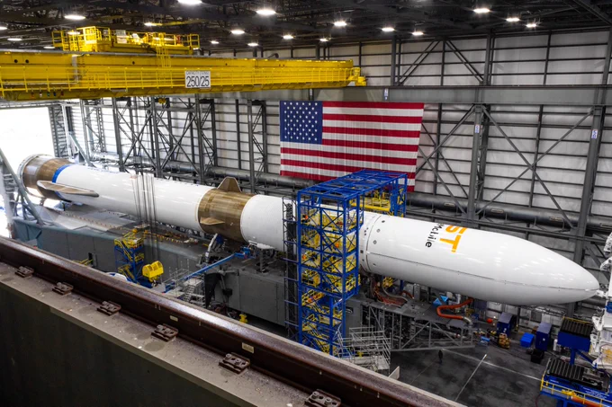 New Glenn is horizontally positioned during payload mate. An American flag hangs on the wall in the background.