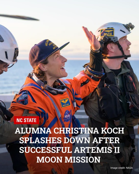Astronaut Christina Koch in an orange spacesuit waves while standing on a ship deck after returning from the Artemis II moon mission.