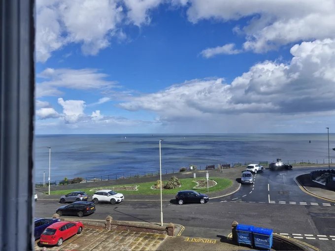 View over a municipal garden towards the sea, with scattered clouds and blue sky. 