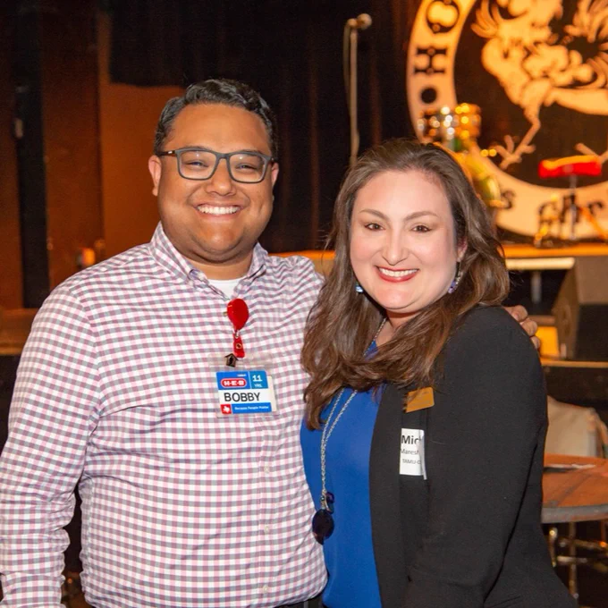 Two TAMU-CC alumni smile and pose for a photo at a mixer event in Corpus Christi, both wear name tags. 