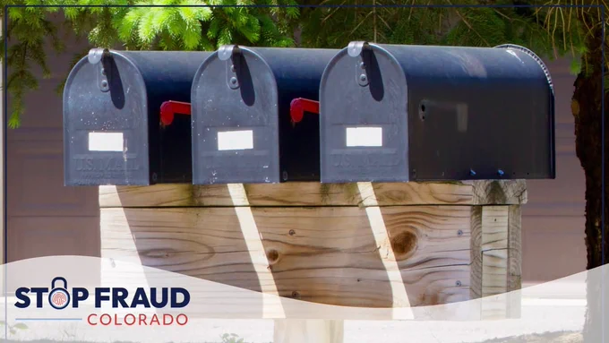 Three U.S. Postal Service mailboxes mounted on a wooden stand with the "Stop Fraud Colorado" logo visible at the bottom.