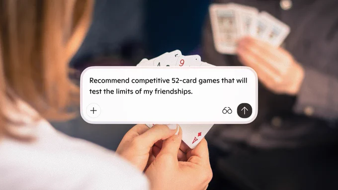 Close-up of hands holding playing cards with a Copilot prompt asking for competitive two-player card games.