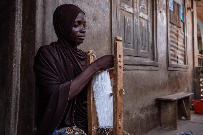Kafat Abdulhakem loops a bundle of thread used in making aso-oke, a handwoven fabric indigenous to the Yoruba ethnic group, in her home workshop in Iseyin, Nigeria. [Toyin Adedokun/AFP]