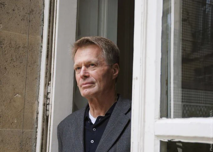 Jean-Marie Gustave Le Clézio standing in a doorway appearing thoughtful.