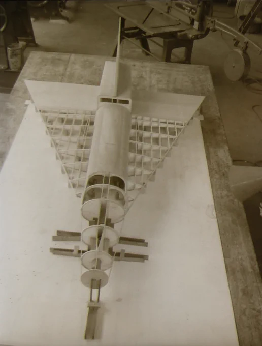 Top-down view of a detailed model airplane with a cylindrical fuselage and lattice wings on a workbench.