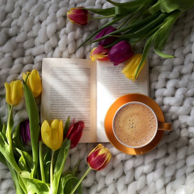 Open book with a cup of coffee surrounded by tulips with a streak of golden light streaming in from a window