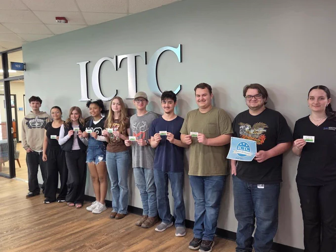Eleven individuals stand in front of a wall labeled "ICTC." They each hold items, possibly awards, and smile.