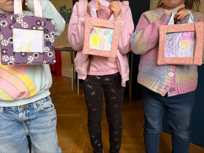 Three children hold up sewn picture frames holding their drawings.