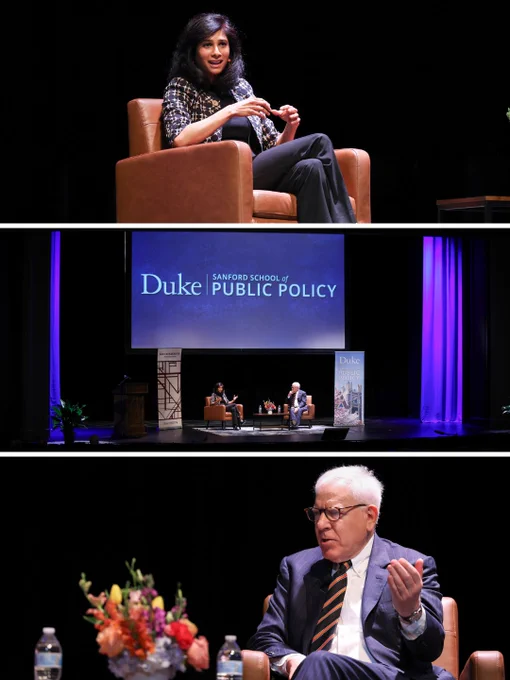 Two people talking while sitting in chairs on stage. Behind them and next to them is signage that says Duke Sanford School of Public Policy.