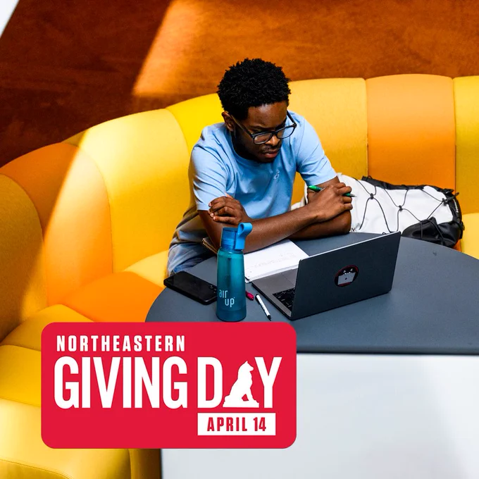 A student sits in Snell Library looking at a laptop. The logo for Northeastern Giving Day on April 14 is in the corner.