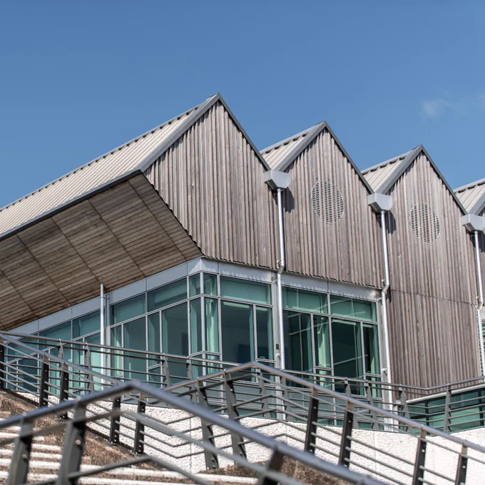 Modern building with angular wooden paneling and large glass windows under a clear blue sky.