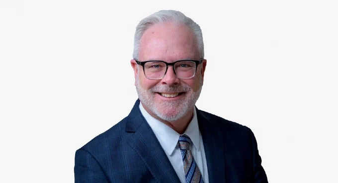 Jerrry Mansfield, VP and Chief Nursing executive smiles in a headshot. He is wearing a blue suit, whit a striped tie. He is smiling directly at the camera.