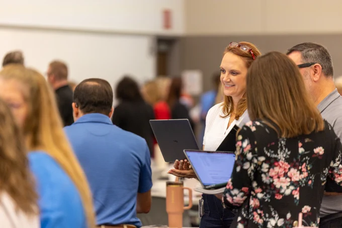A group of ESC staff members is gathered in a room, engaged in conversation. Some are holding laptops. The atmosphere is professional and social.