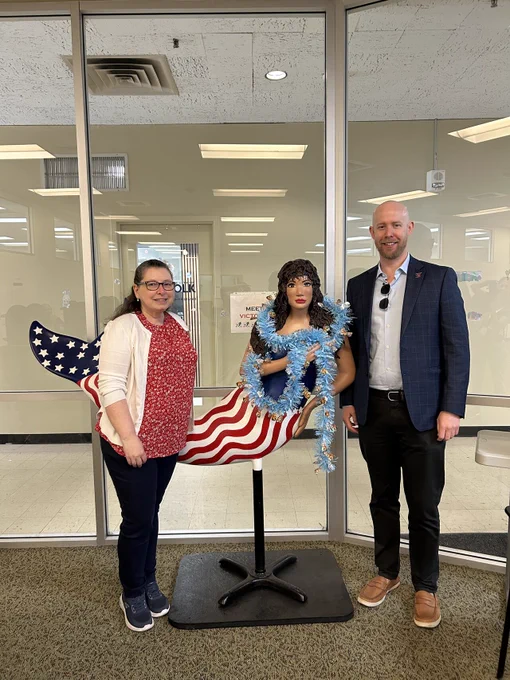 Norfolk registrar Stephanie Iles and Commissioner Steven Koski standing next to a patriotic-themed mermaid sculpture with an American flag design tail and blue garland around her neck.