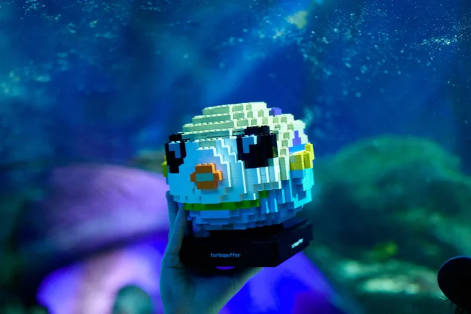 a 3D lego model of turbopuffer’s mascot, puffy, is held up against an aquarium backdrop. puffy is right at home amongst the aquatic life. 