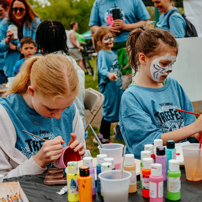 Children focused on painting small pots at an outdoor craft table during a community event.