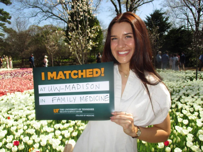 Medical student Alyssa Coley stands in front of flowers and holds an "I Matched!" sign designating her match into the Madison Family Medicine Residency Program.