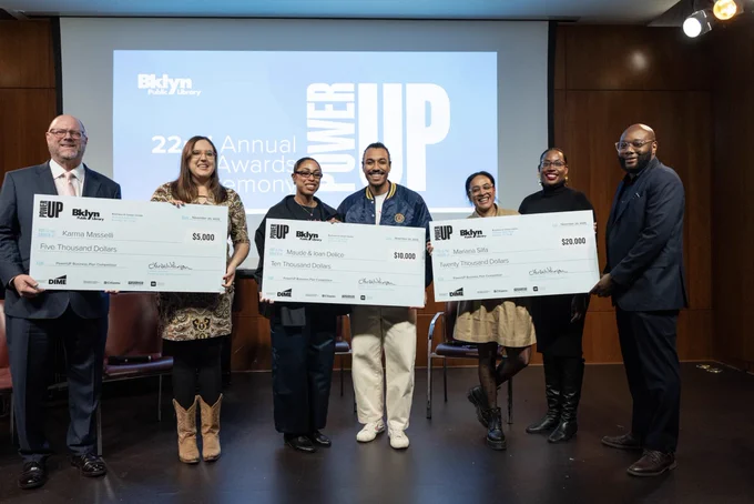 Here's a suitable alt text for the image:

"Six individuals stand side by side holding oversized checks in a room with a Brooklyn Public Library banner in the background. The checks are presented to Kemi Mojole, Meli Maseu & Les Délices, and Mermis 5th, each with different monetary values."