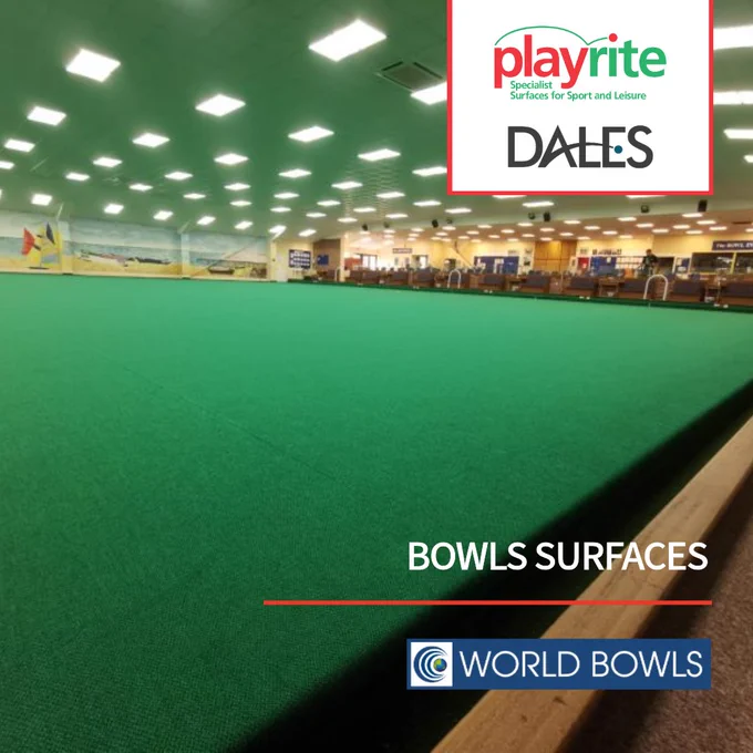 Indoor bowls green surface under bright ceiling lights in a spacious sports hall with wooden walls.