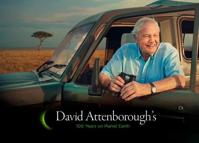 ir David Attenborough leans on the open door of a jeep, smiling and holding binoculars while on location filming for Seven Worlds, One Planet at the Ol Pejeta Conservancy in Kenya. A blue sky dotted with wispy clouds and a lone tree are visible in the background. David Attenborough's 100 Years on Planet Earth is written in text.