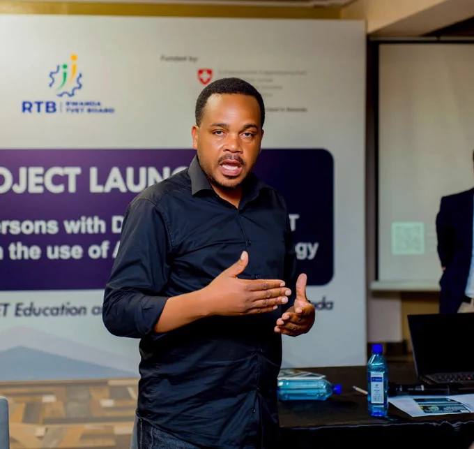 A man in a black shirt gestured with his hands while speaking in front of a project banner