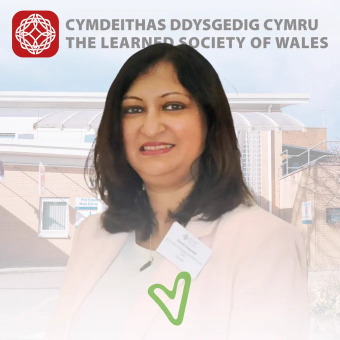 Professional woman wearing a light pink blazer and name badge standing outside a building with The Learned Society of Wales logo above.