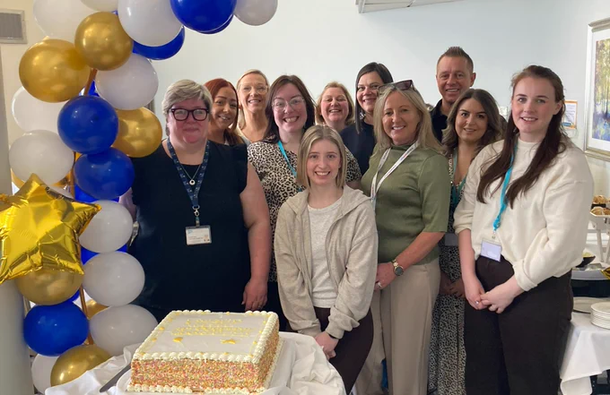 A group of people celebrating with a cake and balloons.