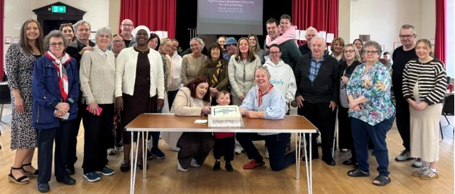 A group of people gathered around a table with a cake.