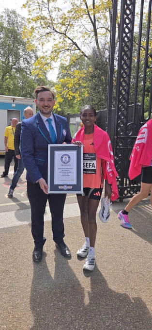 a male adjudicator presents Tigist with her GWR certificate, she's wearing pink running kit