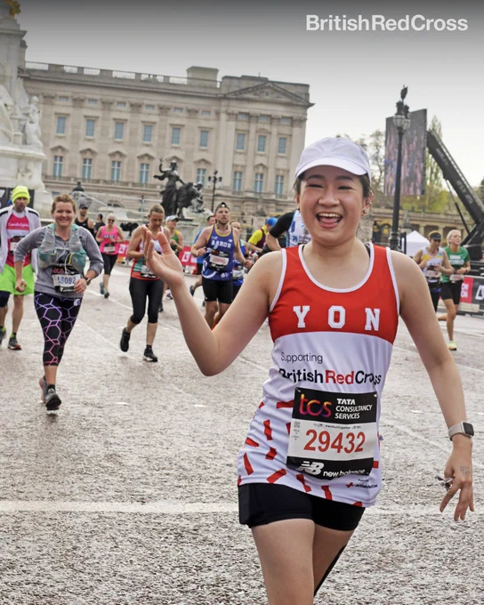 Image of someone running the marathon wearing a British Red Cross vest. They are smiling at the camera and in the background is Buckingham Palace.
