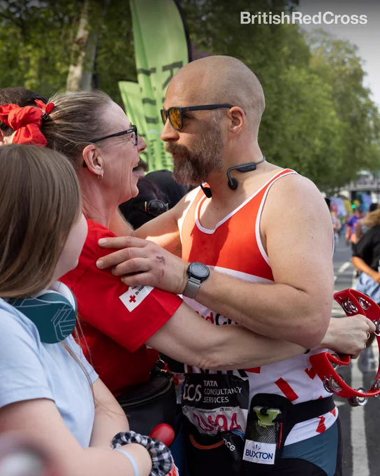 Image of two people embracing on the sidelines. One of them is wearing a British Red Cross running vest and the other is wearing a Red Cross t-shirt. They are looking at each other smiling. 