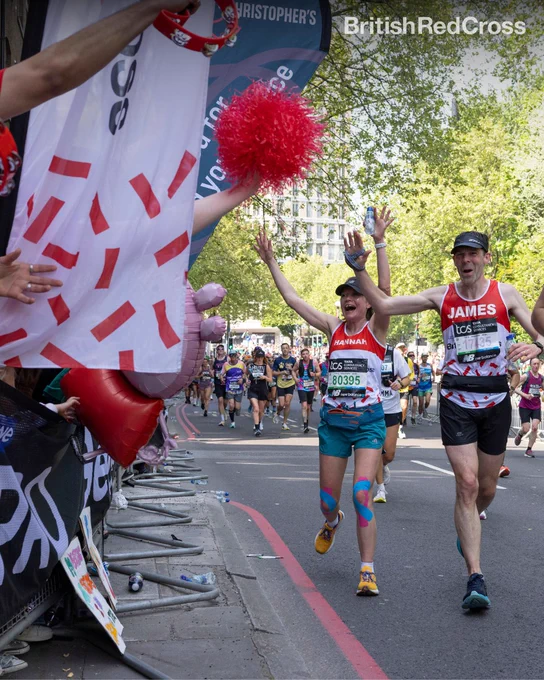 Image of two people running wearing British Red Cross vests and holding up their hands to wave at the British Red Cross supporters at the sidelines.