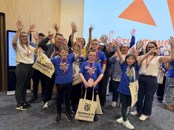 Ninjas (young people), mentors and families from CoderDojo Banbridge standing and waving their hands in celebration at the end of the Coolest Projects event. The young people have their swag bags which say Raspberry Pi Foundation