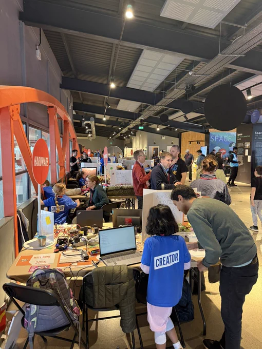 Young people wearing blue T-shirts with ‘Creator’ on the back showing off their tech projects to other young people and adults