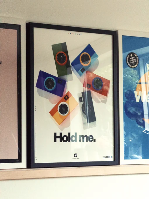 Colorful cameras are arranged in a star pattern on a poster with the text "Hold me." displayed prominently.