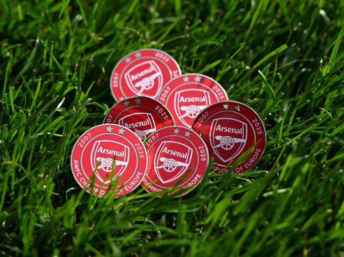 Six of the unique AWFC programme pin badges, nestled in the Emirates Stadium grass