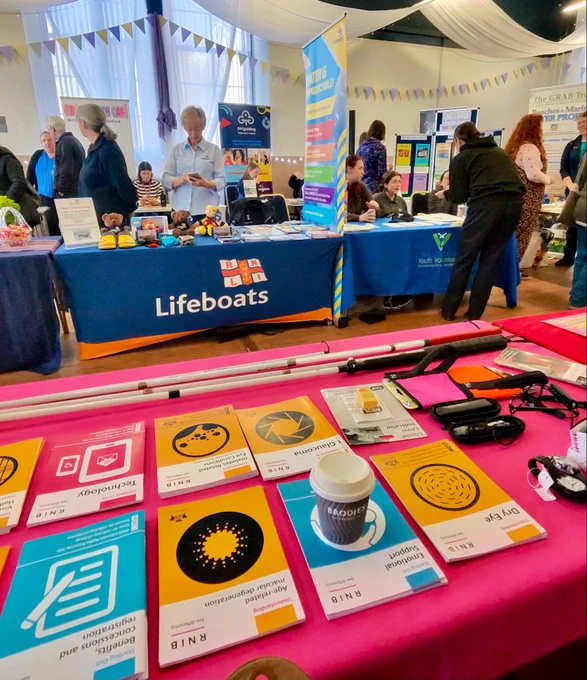 Image using Meta Ray Ban glasses of a RNIB information table with booklets sitting on a pink table cloth