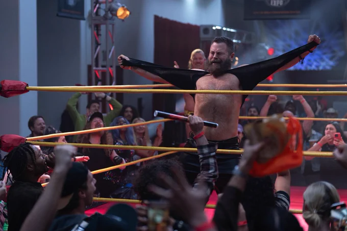 From Margo’s Got Money Troubles. Nick Offerman as Jinx is in the wrestling ring ripping his shirt off as the crowd cheers.
