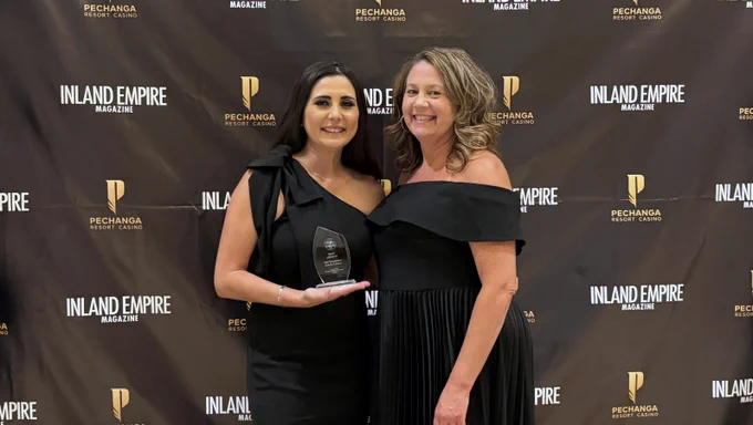 Two individuals pose together in front of a backdrop featuring "Inland Empire Magazine" and "Pechanga Resort Casino" logos. One person is holding an award.