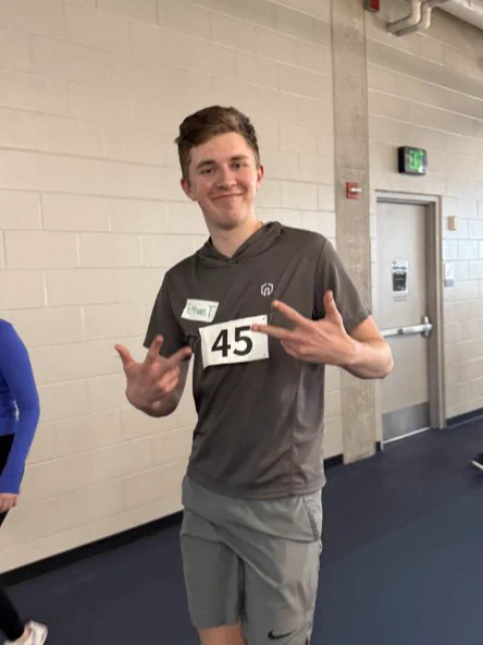 A UI REACH student gives peace signs while running around a track.