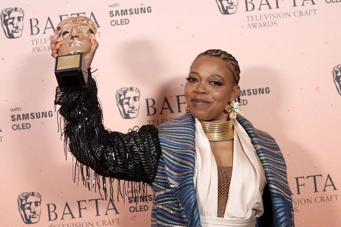 Simone Pennant smiles as she holds her BAFTA up in the air.